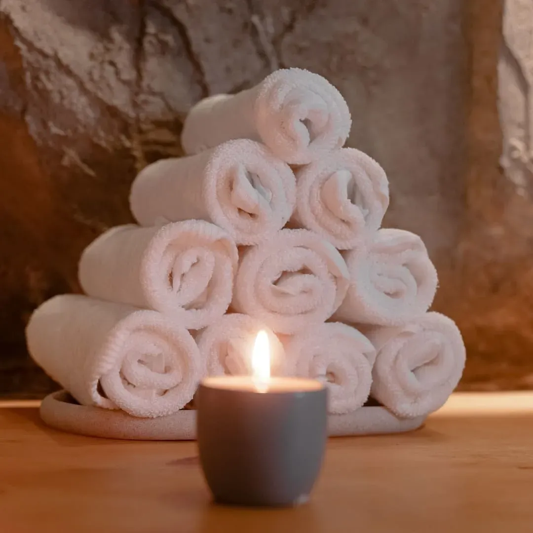 Rolled white towels stacked in a pyramid beside a lit candle