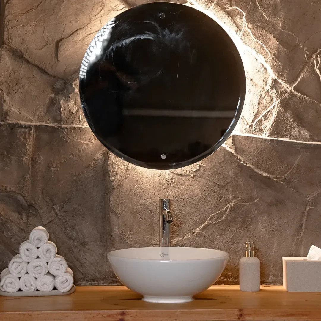 Stone washbasin under a round backlit mirror, with rolled towels