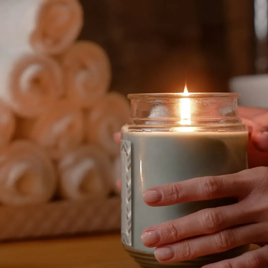 A candle in a glass jar beside rolled towels